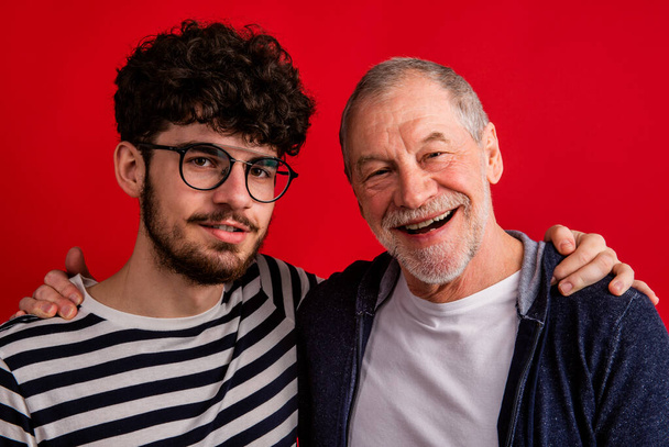 Young man and senior father in a studio on red background. - Photo, Image