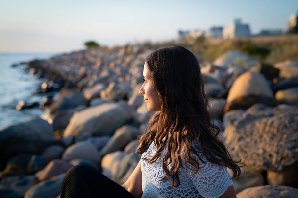Портрет молодой женщины, смотрящей на закат над океаном
 - Фото, изображение