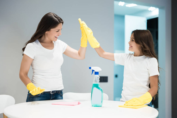 joven hermosa mujer y su linda hija adolescente en guantes amarillos haciendo limpieza de limpiar el polvo con un trapo dando unos a otros alta cinco
 - Foto, imagen