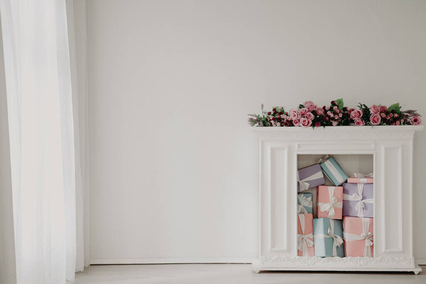 λευκό τζάκι με λουλούδια και δώρα στο εσωτερικό του λευκού δωματίου - Φωτογραφία, εικόνα