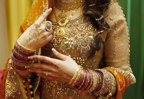 Hermosa novia morena hindú tocar sus pulseras con mehendi de oro y vestido de sari amarillo durante la fiesta de henna
 - Foto, Imagen