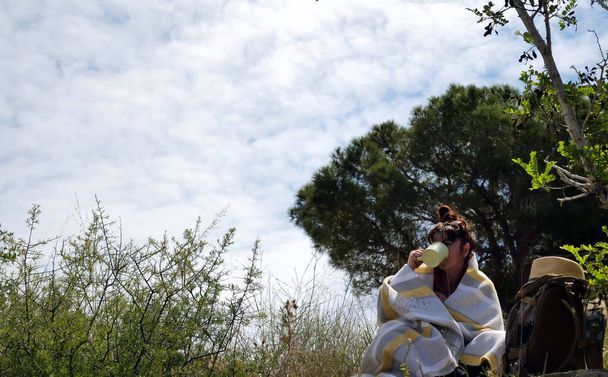 Niza chica turista sentado en la naturaleza envuelto en una manta y beber de una taza
 - Foto, Imagen