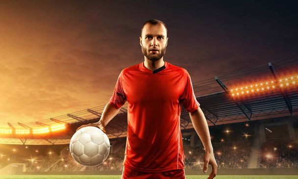 Professionele jonge voetballer met een bal in sportuniform op een veld. Nachtelijke dramatische hemel - Foto, afbeelding