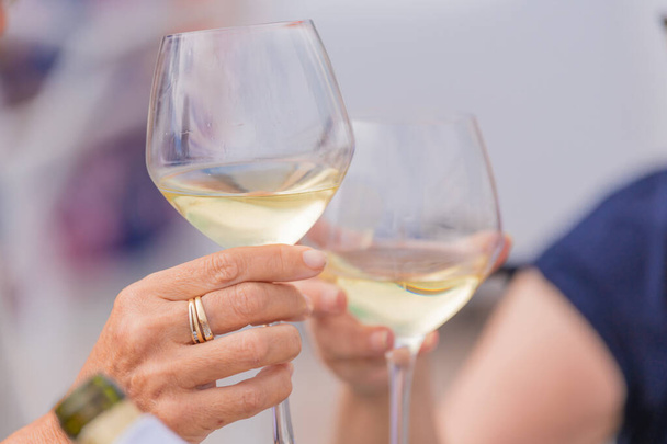 Detalhe da foto de duas mãos juntas segurando dois copos de vinho branco. Conceito de celebração
. - Foto, Imagem