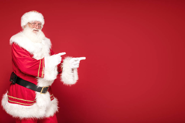Real Santa Claus pointing on red studio background. - 写真・画像