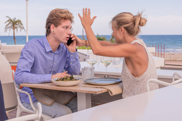 Cute blonde girl trying to take the phone off her boyfriend who speaks on the phone while with the other hand lifts her aggressively. - Photo, Image