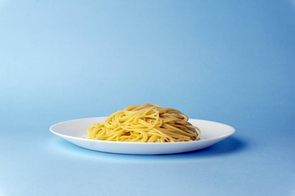 Spaghetti pasta on a white plate on a blue background. Creative, - 写真・画像
