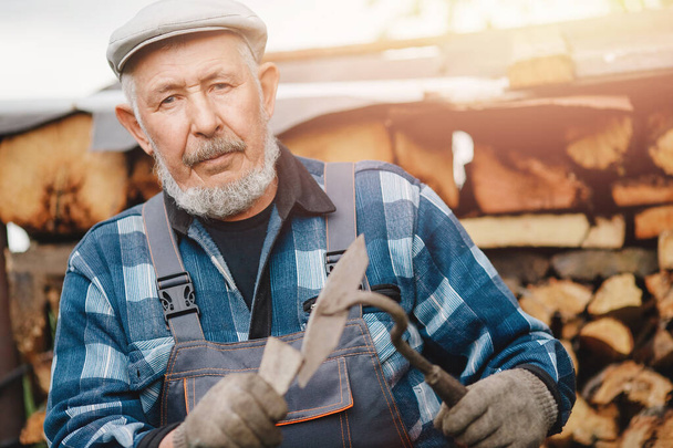 Senior lächelnder Mann schärft Werkzeug für die Bearbeitung von Ackerboden. Landwirtschaftskonzept - Foto, Bild