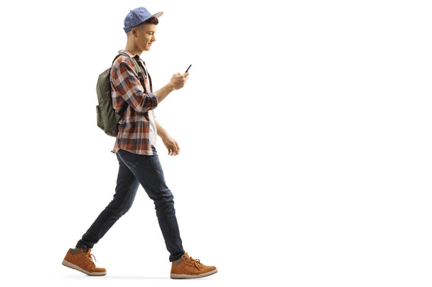 Young guy with a backpack and cap walking and looking at his mob - Photo, image