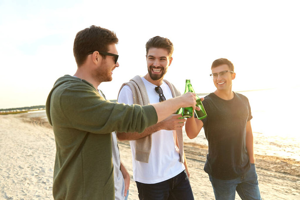 hombres jóvenes brindando cerveza no alcohólica en la playa
 - Foto, imagen