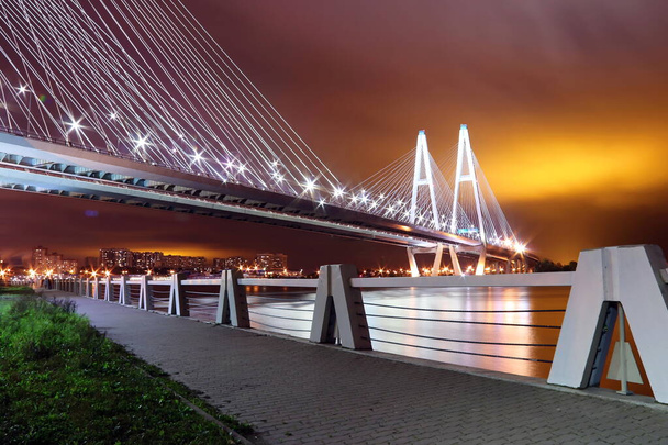 μεγάλο καλώδιο-έμεινε γέφυρα πάνω από το ποτάμι τη νύχτα με πολύχρωμο φωτεινό φωτισμό - Φωτογραφία, εικόνα