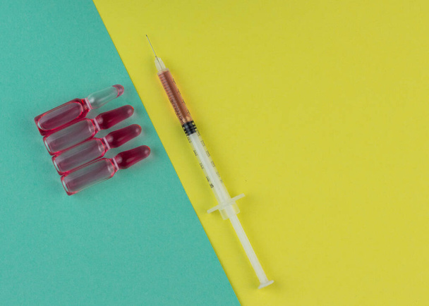 Ampoule and syringe with red liquid on colorful background. Flu vaccination. Catch-up immunization. - Фото, зображення