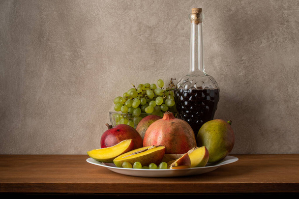 Mango, granat, winogrona i butelka wina. Martwa natura na szarym tle - Zdjęcie, obraz