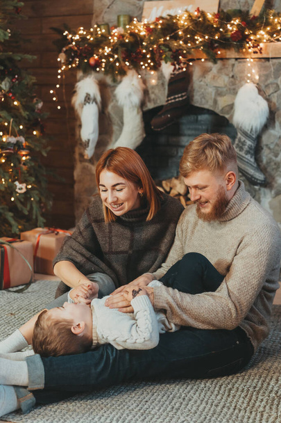 Young caucasian family mom dad son near fireplace christmas tree - Photo, Image