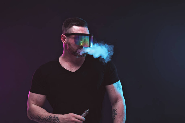 Men with beard in sunglasses vaping and releases a cloud of vapor - Foto, afbeelding