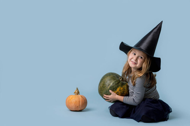 Little witch plays with pumpkins sitting on the floor - Foto, afbeelding