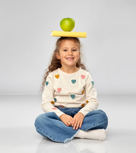 little girl with book and apple sitting on floor - Фото, изображение