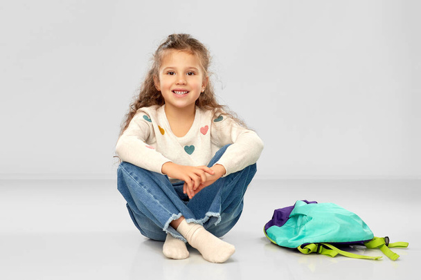 happy little girl with school bag sitting on floor - Foto, Imagem