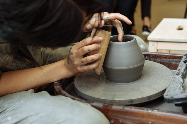 De meester creëert producten van grijze klei op het wiel van een Potter. Meisje creëert een keramische vaas - Foto, afbeelding