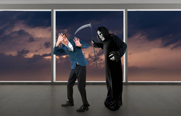 Man in a Halloween grim reaper ghost costume chasing, mocking and making fun of scared businessman running away.  Can also depict death following a man as a metaphor for life insurance.  - Photo, Image
