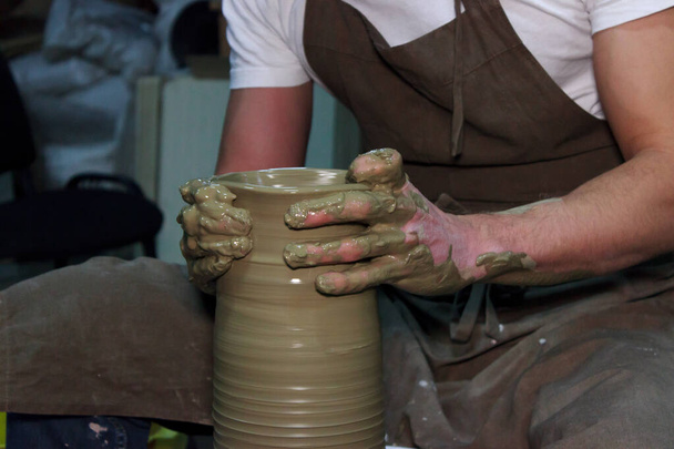 ervaren pottenbakker maakt een grote vaas op een pottenbakkerswiel. kleiproduct. handen van een pottenbakker. reportage schieten. - Foto, afbeelding