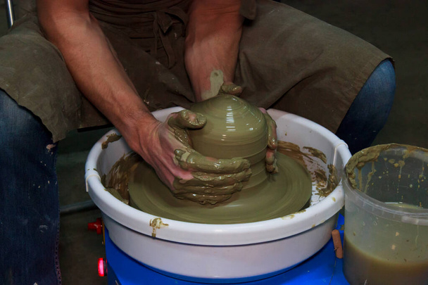 experienced potter makes a large vase on a potter's wheel. twisting a narrow neck. clay product. hands potter. reportage shooting. work with large piece of clay - Photo, Image
