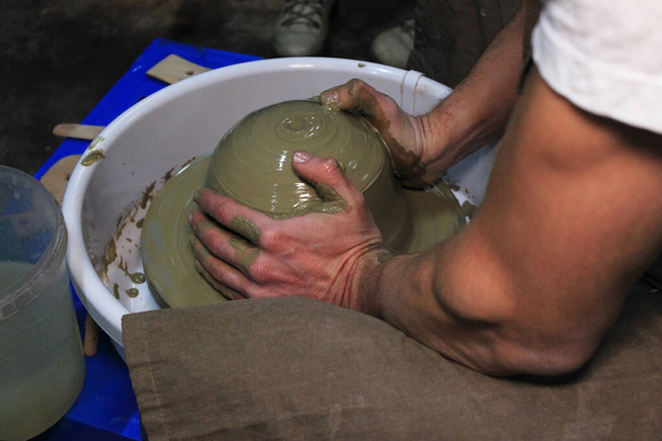 experienced potter makes a large vase on a potter's wheel. twisting a narrow neck. clay product. hands potter. reportage shooting. work with large piece of clay - Photo, Image
