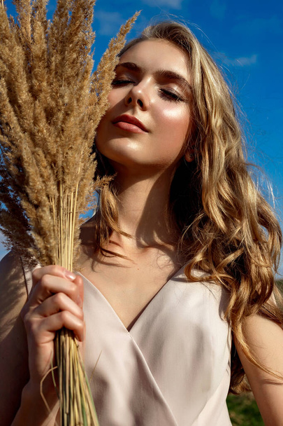 Portrait of a blonde young girl model who stands and poses on a sunny day against a background of haystacks and blue sky - Photo, image