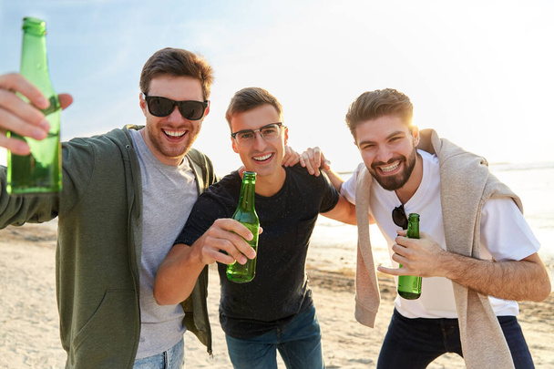 young men toasting non alcoholic beer on beach - Fotó, kép