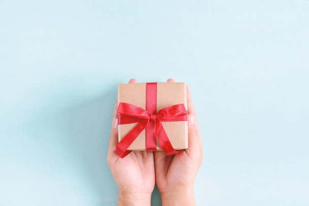 Mãos segurando caixa de presente com fita vermelha para dar no fundo pastel
 - Foto, Imagem