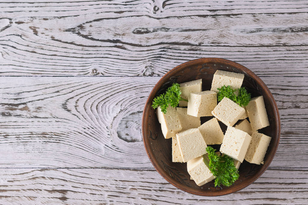 Parsley with slices of tofu cheese in a clay bowl on a wooden table. Soy cheese. Flat lay. - Photo, Image