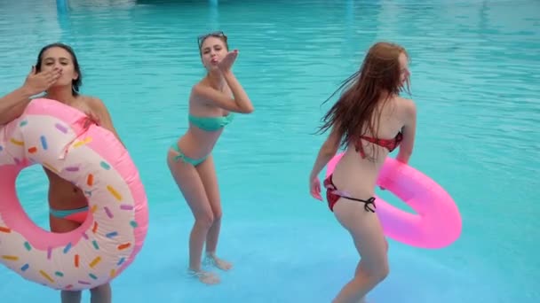 mejores amigos en traje de baño bailan en la piscina con agua azul, verano, chicas alegres con anillos inflables rosados
 - Metraje, vídeo