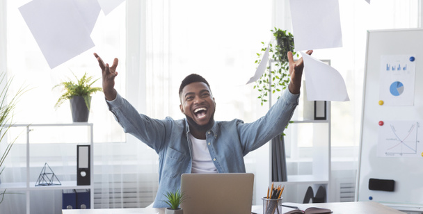 Alegre empleado afroamericano celebrando éxito tirando papeles en la oficina
 - Foto, Imagen