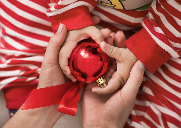 赤いクリスマスボールを手に持っている赤ちゃんとお母さん - 写真・画像
