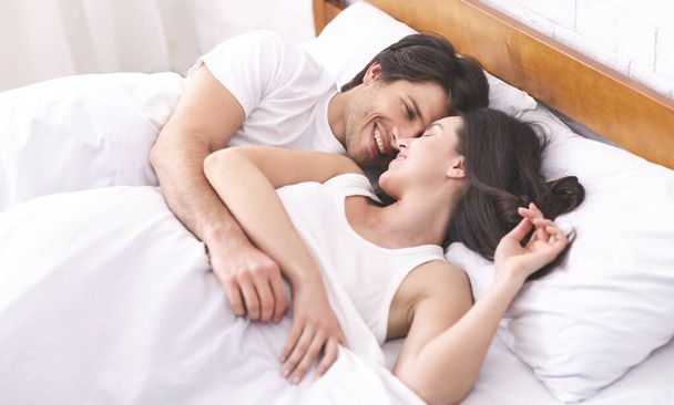 Cheerful millennial man and woman waking up together in bed - Foto, imagen