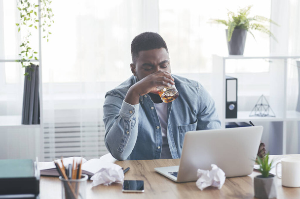 Empleado afroamericano cansado bebiendo alcohol en el lugar de trabajo
 - Foto, imagen