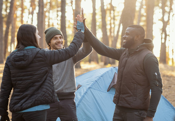 Веселые друзья, собирающие руки над палаткой для кемпинга
 - Фото, изображение