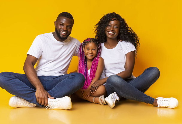 Ritratto di gioiosa famiglia africana di tre persone sedute al piano terra
 - Foto, immagini