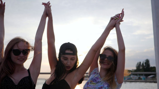 χαρούμενες φίλες χορεύουν στο ηλιοβασίλεμα στην παραλία, τρεις γυναίκες σηκώνουν τα χέρια ψηλά στην παραλία, καλοκαιρινό βράδυ - Πλάνα, βίντεο