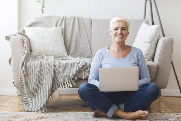 Active old woman sitting on floor and using laptop - Photo, Image