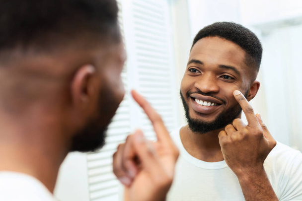 Alegre hombre negro aplicando crema de mimos en la cara en el baño
 - Foto, Imagen