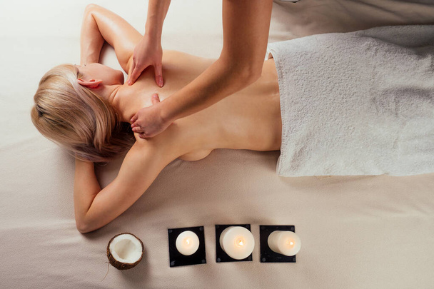 Ayurvedic relaxing.health beauty happy blonde woman in spa salon getting massage .Beautiful girl enjoying day spa resort, lying down on the table treatment procedure next to the candle fire - Photo, Image