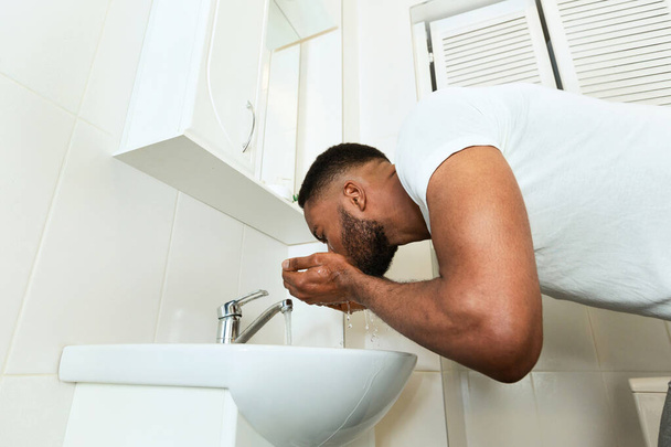 Africano lavándose la cara en el baño
 - Foto, imagen
