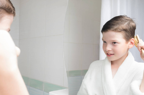 boy in bathrobe combing hair in bathroom in the morning - Φωτογραφία, εικόνα