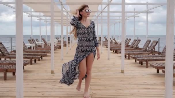 young woman glasses walks on wooden pier, Expensive holidays of women on coast ocean, female in sunglasses - Materiał filmowy, wideo