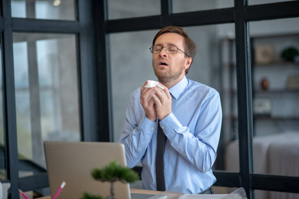 Dark-haired office worker standing near laptop and sneezing - Fotografie, Obrázek