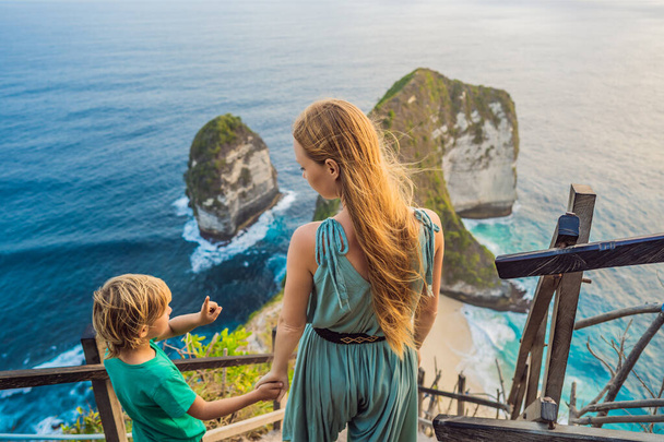 Family vacation lifestyle. Happy mother and son stand at viewpoint. Look at beautiful beach under high cliff. Travel destination in Bali. Popular place to visit on Nusa Penida island - Valokuva, kuva