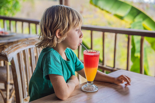 Boy drinks two tone cocktail in a glass in the cafe - Zdjęcie, obraz