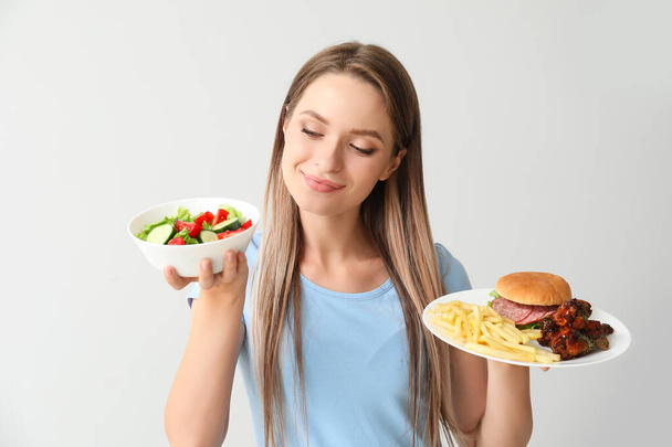 Žena se zdravou a nezdravou stravou na světlém pozadí. Dietní koncept - Fotografie, Obrázek