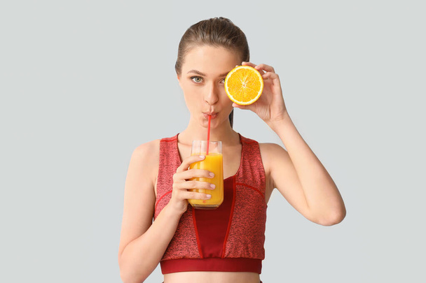 Sporty woman drinking healthy orange juice on light background. Diet concept - Fotoğraf, Görsel